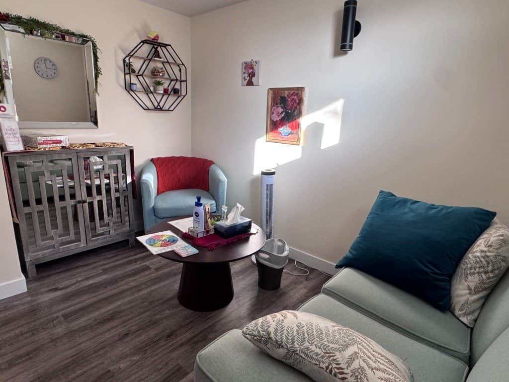 A bright counselling room with a sofa, cushions and a red armchair